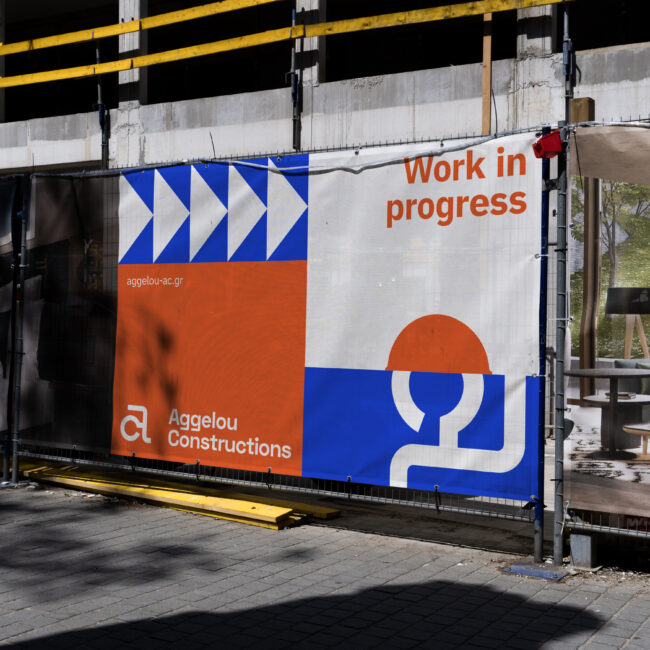 Aggelou Constructions site hoarding in the new blue-and-orange identity, reading ‘Work in progress’